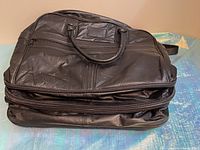 Folded black leather duffel bag with visible zipper and leather creasing, showing wear.