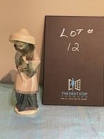 Side view of vintage Lladro figurine showing woman standing carrying a child on her back with broad hat and robe.