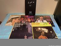 Top view of five vinyl record album covers laid out side by side showing titles and artists, indicating lot contents.