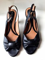 Top view of pair of black leather sling-back pumps showing open toe and bow detail on upper.