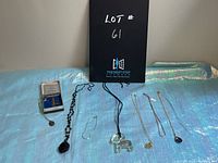 Photo showing seven assorted costume jewelry items, including pendants and necklace, on a light blue reflective surface with a black stand displaying lot number.
