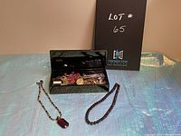 Lot contents showing two necklaces laid out in front of an open black jewelry box filled with assorted jewelry pieces and loose stones.