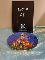 Photo of the collectible Royal Doulton plate "Columbine" showing the full colorful design on a blue background with artistic depiction of a lady in a colorful dress.