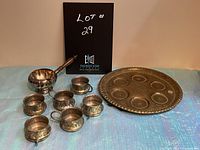 Photo showing the full set of one metal Seder plate, six matching cups, and a silver creamer with wooden handle