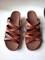Top view showing tan vegan leather criss-cross straps with floral cutout details and cushioned insole with Skechers logo.