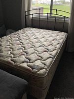 Full view of metal bed frame with mattress and box spring in a room near window, carpeted floor.