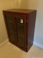 Front angled view of wooden cabinet showing two glass doors and bottom drawer