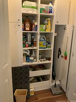 Wide view of white cabinet with shelves and drawers filled with multiple cleaning products, compostable bags, bottles, and assorted household items.