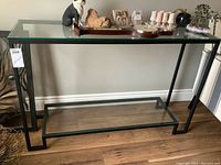 Full front view of the metal framed console table with glass inserts, showing the entire structure and glass shelves.