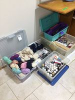 Photo showing multiple plastic storage totes filled with assorted craft supplies including yarn skeins, sewing threads, paint brushes, glue sticks, and decorative ribbons.