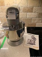 Photo of gray Cuisinart stand mixer with stainless steel bowl on countertop next to instruction manual.