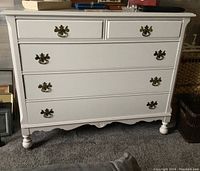 Front view showing entire white painted dresser with four drawers and ornate metal pulls.