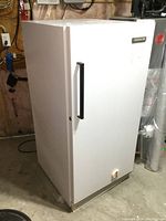 Front and right side view of white Kelvinator upright freezer with black handle and temperature dial at bottom front.