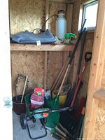 Wide view of shed corner showing Scotts garden seeder, shovels, rake, pruning clippers, and other tools gathered together