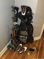 Photo showing Lopez branded black and brown golf bag filled with various Wilson golf clubs, with a golf cart and men's golf shoes in front.