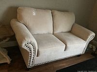 Front view of beige chenille loveseat showing rolled arms and nailhead trim