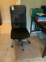 Full view of black office chair with fabric seat and mesh backrest, showing padded upper section of backrest and five rolling caster wheels on carpet.