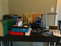 Fellowes paper shredder, framed cork board, envelopes, stapler, tape dispenser and other office supplies on black table.