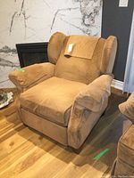 Brown upholstered recliner chair angled view showing fabric covers on arms and headrest, wooden legs visible.