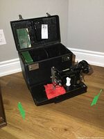 Singer sewing machine mounted in open black carrying case on hardwood floor