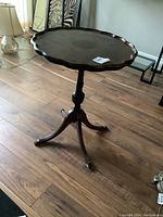Side view of the wooden side table with scalloped edge top and pedestal base with claw feet.