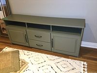 Front view of a painted green wooden sideboard showing two drawers in the center below three open shelves, flanked by two cabinet doors.