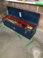 Blue portable metal toolbox filled with various hand tools including hand planes and saws, open lid showing interior compartments.