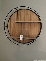 Full view of round wall shelf, black metal frame with wood backing and multiple shelf compartments.