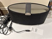 Photo of a black fabric covered Bowers & Wilkins oval speaker with reflective top surface and attached power cable.