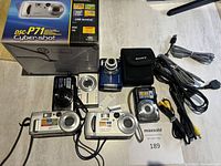 Six Sony Cyber-shot cameras with original DSC-P71 box, carrying case and cables on table