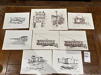 Photo showing nine black and white prints arranged on wooden surface. Subjects include buildings, trams, and rural scenes.