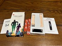 Photo of fitness tracker device, replacement wrist bands in peach and orange, product box and instruction manual on wood surface
