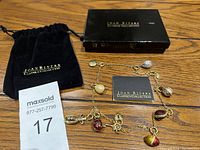 A Joan Rivers Classics Collection charm necklace with assorted charms in different colors and shapes, accompanied by a branded black suede pouch, a black box with gold lettering, and an information card, displayed on a wooden surface.