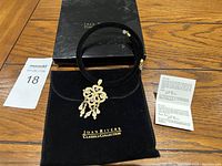Joan Rivers Classics Collection necklace displayed with its original black box, black pouch, and informational card on a wooden floor.