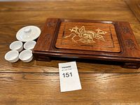 Wooden tea tray with floral inlay and carved details shown with white ceramic tea set including 1 lidded teapot and 4 small cups