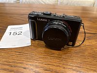 Front angled view of the black Lumix camera, lens cap attached on lens.