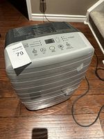 Grey Noma dehumidifier with visible control panel and attached power cord on hardwood floor near staircase.