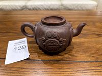 Front view of purple clay teapot showing handle, spout, and embossed decoration on body.