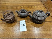 Front view of three purple clay teapots on a wooden surface showing their shapes and details.