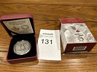 Photo of the silver coin in a red leather case, accompanied by the original decorative box and auction tag.