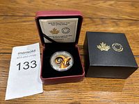 2015 $5 fine silver coin with colored ram's head design in maroon presentation box, black outer box, and certificate of authenticity shown.