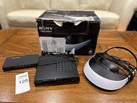 Sony HMZ-T2 Personal 3D Viewer headset, passthrough box, HDMI splitter, and packaging box on wooden table