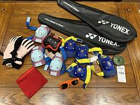 Photo showing all sport protective pads, gloves, wrist support, sunglasses, and two Yonex badminton racket bags laid out on a wooden surface.