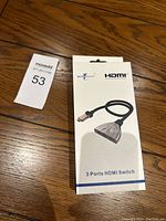 Photo of the 3 Ports HDMI Switch retail box on wooden floor with a lot tag visible nearby.