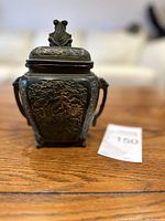Front angled view of the bronze incense burner showing detailed relief work and decorative finial on lid.