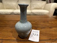 Single small vintage Chinese porcelain vase on wooden surface with auction tag number 123 beside it.