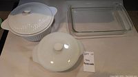 Three items on table: two white lidded ceramic dishes and one clear rectangular Pyrex glass baking tray.