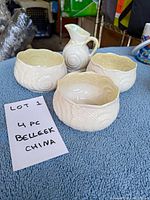 Four pieces of Belleek china including three small bowls and one creamer, all with shell design, arranged on a blue towel with a label.