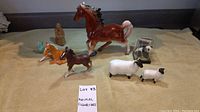 Overview of all figurines including horses, sheep, panda in a case, and small brown seated figure on a plain surface.