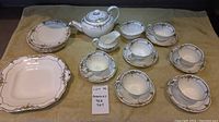Full tea set laid out on beige surface showing teapot, teacups with saucers, creamer, sugar bowl, and serving plates.